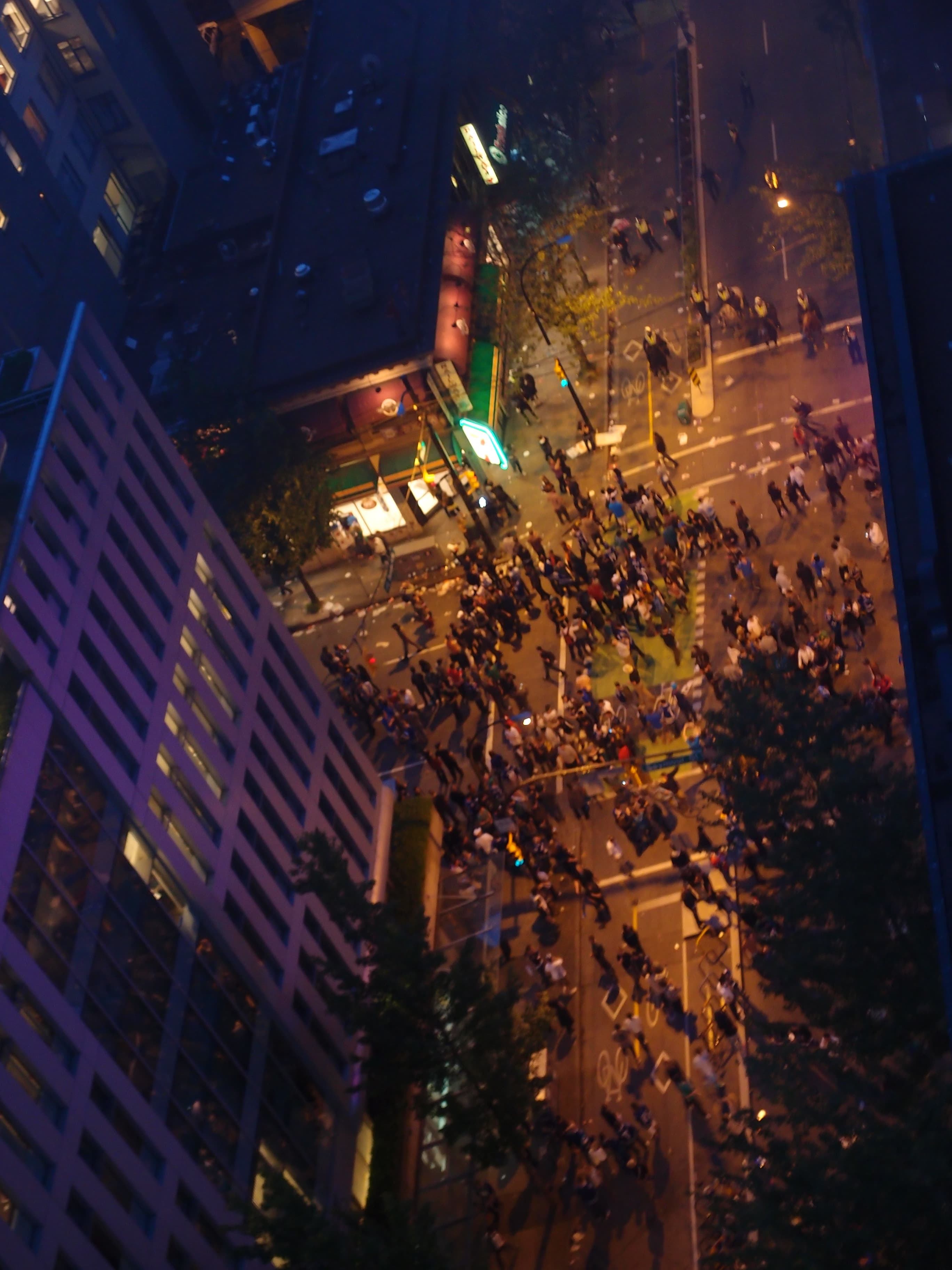 Crowd-filled downtown Vancouver intersection seen from above during civil unrest at night.